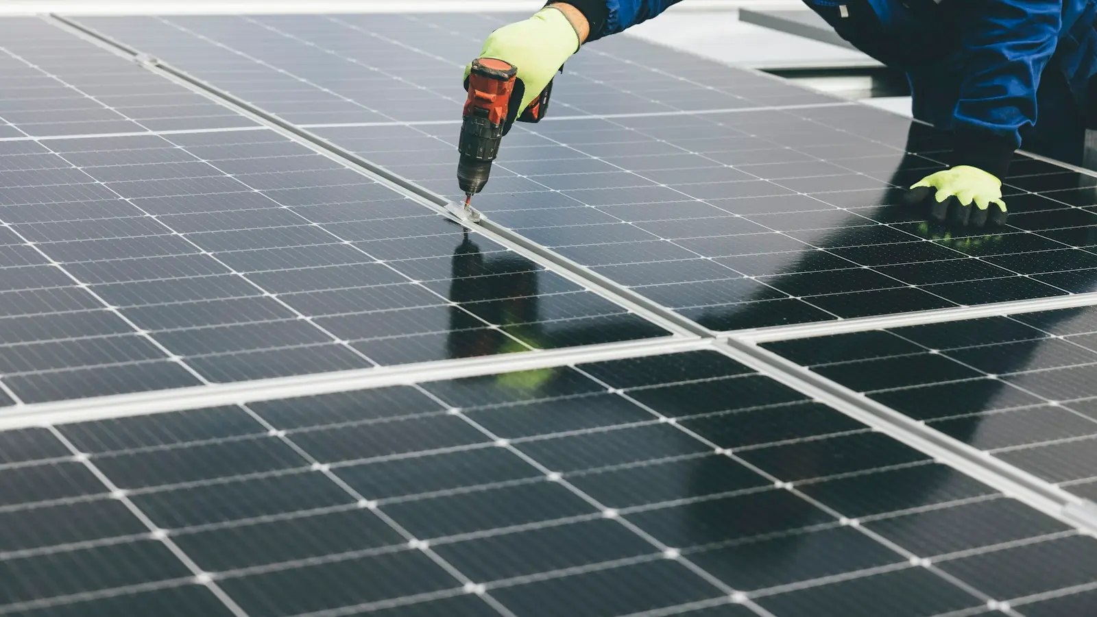 Installateur met werkhandschoenen schroeft een zonnepaneel vast